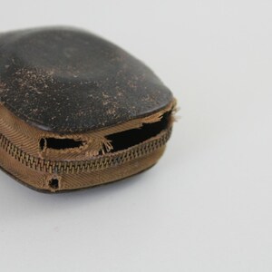 Puede incluir: Una peque&ntilde;a caja de cuero marr&oacute;n con cierre de cremallera. La cremallera est&aacute; parcialmente abierta y la caja est&aacute; ligeramente desgastada.