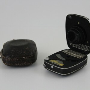 Puede incluir: Un fot&oacute;metro negro y plateado con una funda de cuero. El fot&oacute;metro est&aacute; abierto y la lente es visible. El fot&oacute;metro tiene una variedad de marcas y n&uacute;meros.