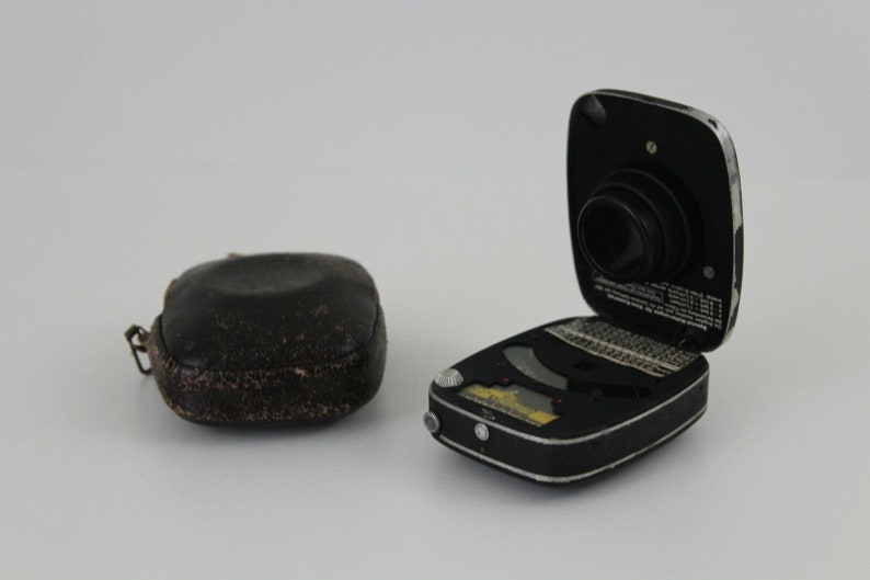 Puede incluir: Un fot&oacute;metro negro y plateado con una funda de cuero. El fot&oacute;metro est&aacute; abierto y la lente es visible. El fot&oacute;metro tiene una variedad de marcas y n&uacute;meros.