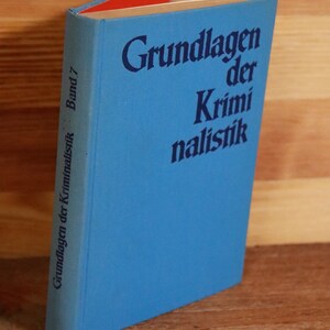May include: A blue book with the title "Grundlagen der Kriminalistik" and the subtitle "Band 7" printed on the spine.