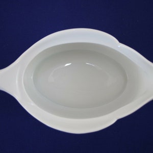 Puede incluir: Salsera de porcelana blanca con un interior liso y redondeado y un borde ligeramente acampanado. La salsera tiene una sola asa en el lado izquierdo.
