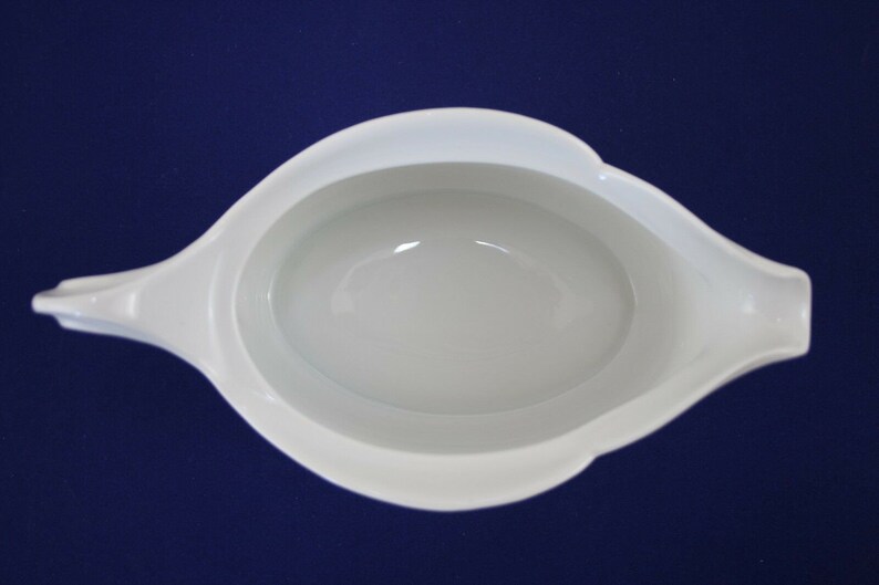 Puede incluir: Salsera de porcelana blanca con un interior liso y redondeado y un borde ligeramente acampanado. La salsera tiene una sola asa en el lado izquierdo.