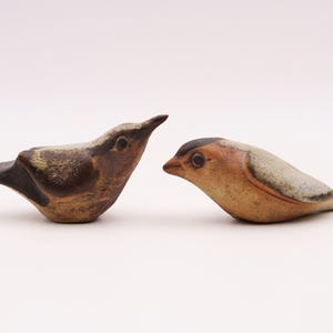 Könnte beinhalten: Zwei Keramik-Vogelfiguren, eine braun und weiß mit einem langen Schnabel, die andere braun und grau mit einem kurzen Schnabel.