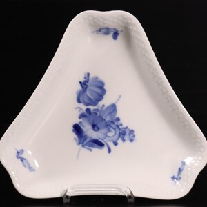 Op de afbeelding: Witte driehoekige porseleinen schaal met een blauw bloemmotief. De schaal heeft een geweven rand en een centrale cluster van blauwe bloemen met bladeren. Kleine bloemaccenten zijn op elke hoek geplaatst.
