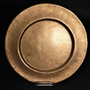 Peut inclure: Une assiette ronde en métal de couleur dorée avec un bord légèrement surélevé. L'assiette a un aspect usé et vieilli avec une surface texturée.