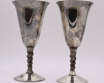 Puede incluir: Dos copas de plata con la parte superior acampanada y un diseño de tallo retorcido. Las copas tienen una base ancha y un acabado pulido. El tallo presenta un intrincado patrón en espiral. Las copas son probablemente vintage o antiguas.