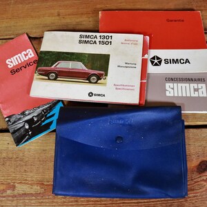 Può includere: Una collezione di manuali per auto Simca d'epoca e una cartella in vinile blu. I manuali sono in francese e tedesco e presentano i modelli Simca 1301 e 1501. La cartella ha il logo Simca.