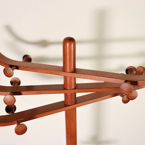 Puede incluir: Un perchero de madera con cuatro brazos curvos y una base redonda. Los brazos están unidos a un poste central y tienen pomos redondeados en los extremos.