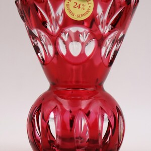 Könnte beinhalten: Eine kleine, rote Kristallvase mit rundem Boden und ausgestelltem oberen Rand. Die Vase ist mit einem geschliffenen Glasmuster verziert. Die Vase trägt ein goldenes Etikett mit der Aufschrift "Bleikristall Bavaria 24% Germany".