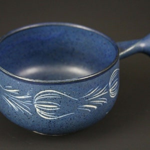 Può includere: Una ciotola in ceramica blu con un motivo floreale bianco e un manico. La ciotola è macchiata di blu e bianco.