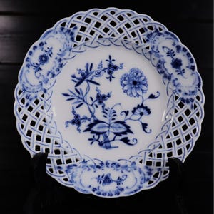 Könnte beinhalten: Ein weißer Porzellanteller mit blauem Blumendesign und einem spitzengleichen Rand. Der Teller ist mit einem zarten Blumenmuster in Blautönen verziert.