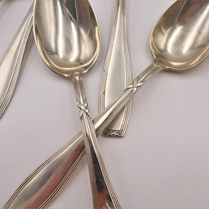 May include: A set of five silver spoons with intricate designs on the handles. The spoons are arranged in a criss-cross pattern, showcasing their polished surfaces.