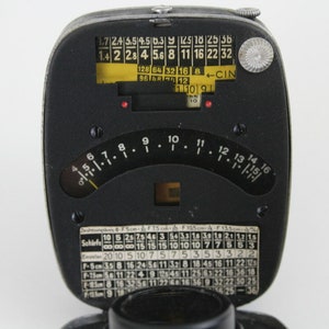 Puede incluir: Un fot&oacute;metro negro y plateado con un dial circular y una etiqueta amarilla con el texto "1.7 2.4 5.5 4 5.6 8 11 16 22 32 128 64 32 16 8 - CIN 96 16 10 10 10". El dial tiene marcas para los diafragmas y las velocidades de obturaci&oacute;n. El fot&oacute;metro tambi&eacute;n tiene una peque&ntilde;a ventana para ver la luz.