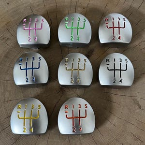 Puede incluir: Siete pomos de palanca de cambios plateados con patrones de cambio de color. Los patrones son en rosa, verde, rojo, azul, dorado, negro y amarillo. Cada pomo tiene los números R, 1, 3, 5, 2 y 4.