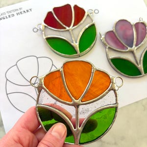 Pode incluir: Pingentes de flores em vitrais coloridos em tons de vermelho, laranja e roxo. Cada peça apresenta um design floral com folhas verdes e detalhes brancos, emoldurado em prata. O texto "Spring Flower Minis" é visível.