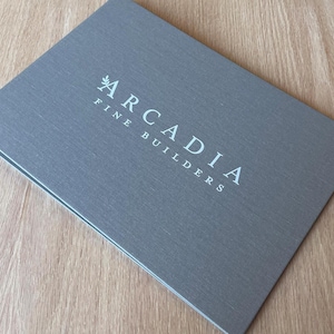 May include: A gray, textured, rectangular brochure with the text "ARCADIA FINE BUILDERS" printed in white.