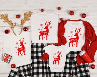 May include: A family of four matching Christmas pajamas with red reindeer designs and personalized names: Papa, Mama, Emily, and Charlie. The pajamas are white with black and white plaid pants.