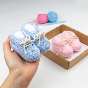 May include: Two pairs of crocheted baby shoes, one pair is blue and the other pair is pink. The shoes have white laces and are in a cardboard box.