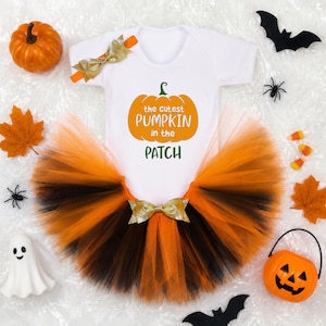 Könnte beinhalten: Ein weißer Kurzarm-Body mit dem Text "the cutest PUMPKIN in the PATCH" und einem Kürbis-Motiv, kombiniert mit einem orange-schwarzen Tüll-Tutu mit goldener Schleife sowie einem passenden Stirnband mit goldener Schleife, umgeben von Halloween-Deko.