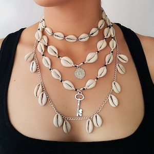May include: Layered necklace with white shell charms and a silver key pendant. The necklace is made of silver chain and black beads.