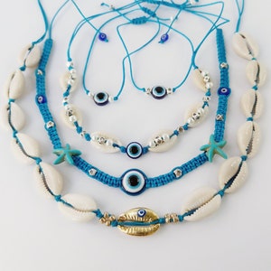 Puede incluir: Un conjunto de cuatro collares de color azul turquesa con conchas blancas y dijes de ojo azul. Los collares están superpuestos y presentan diferentes estilos, incluyendo un collar de cuentas con perlas blancas y un collar con un dije de estrella de mar.