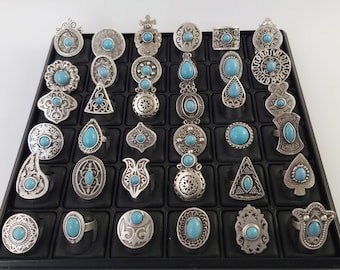 May include: A display of 36 silver rings with turquoise stones. The rings are arranged in a grid pattern on a black display stand.