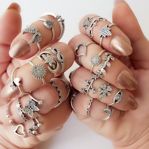 May include: A set of silver rings with various designs, including stars, moons, hearts, butterflies, and leaves. The rings are stacked on multiple fingers.
