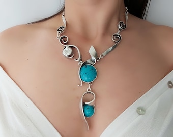 May include: A silver statement necklace with a turquoise stone pendant. The necklace features a delicate, swirling design and a smaller clear stone accent.