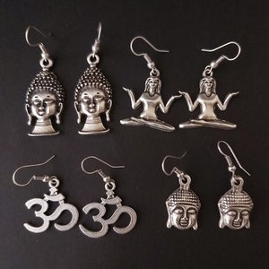 Puede incluir: Un conjunto de ocho pendientes de plata con varios símbolos budistas e hindúes. Los pendientes incluyen dos pares de pendientes con una cabeza de Buda, dos pares de pendientes con un Buda sentado y dos pares de pendientes con el símbolo Om.