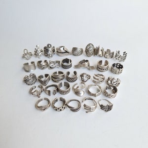 May include: A collection of 30 silver toe rings with various intricate designs. The rings are arranged in a semi-circle on a white background.