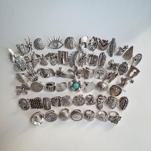 Könnte beinhalten: Eine Sammlung von Silberringen mit verschiedenen Designs, darunter geometrische Formen, Tiere und abstrakte Muster. Einige Ringe haben türkisfarbene Steine.