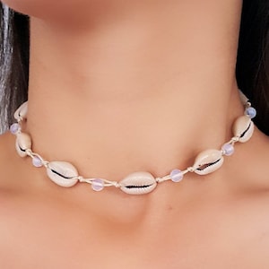 May include: A delicate choker necklace made with natural seashells and small lavender beads. The necklace is strung on a thin white cord.