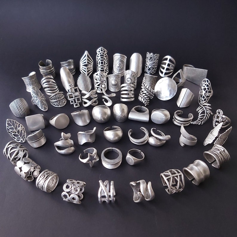 May include: A collection of silver-toned rings with intricate designs. The rings are arranged in a circle on a black background.