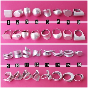 May include: A collection of 16 silver rings in various shapes and sizes. The rings are arranged in three rows, with the first row containing 8 rings, the second row containing 8 rings, and the third row containing 8 rings.