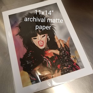 May include: An 11x14 inch print on archival matte paper. The artwork features a person with black hair, wearing a black outfit, and making a rock and roll hand gesture. The person is wearing makeup and has their mouth open.