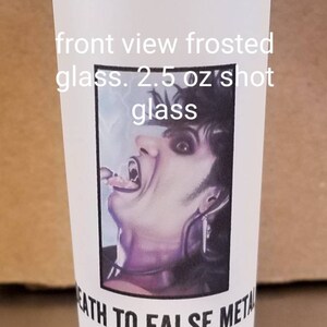 May include: A white frosted glass shot glass with a black and white image of a person with fangs and the text "Death to False Metal". The glass is 2.5 oz.