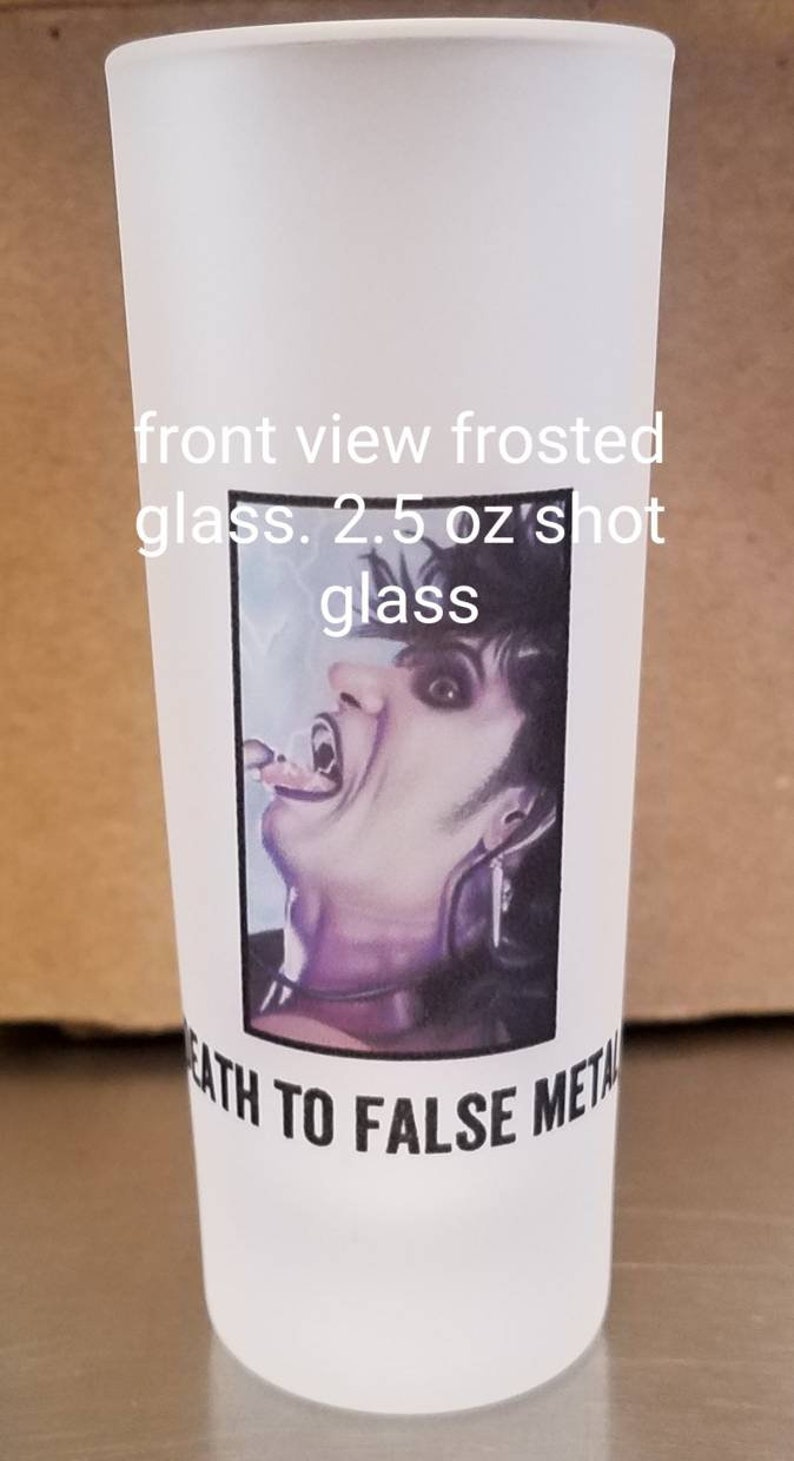 May include: A white frosted glass shot glass with a black and white image of a person with fangs and the text "Death to False Metal". The glass is 2.5 oz.