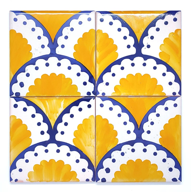 May include: Four square ceramic tiles arranged together. Each tile features a repeating pattern of a yellow fan shape, a white scalloped edge with blue dots, and a blue curved border. The background is white.