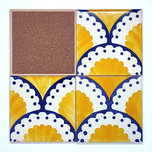 May include: Four square ceramic coasters with a decorative floral design. The coasters feature a yellow and blue pattern on a white background. One coaster has a cork backing.
