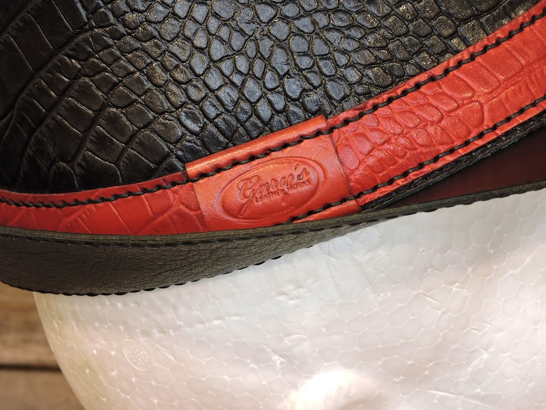 K&ouml;nnte beinhalten: Nahaufnahme eines schwarzen Lederriemens mit roten N&auml;hten und einem roten Lederflicken mit dem in Wei&szlig; gepr&auml;gten Text "Garcia's Leather Works".