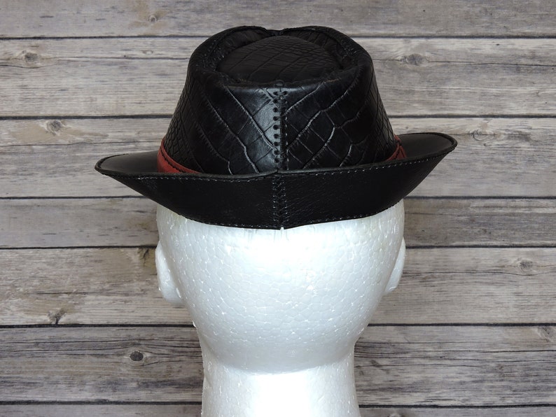 K&ouml;nnte beinhalten: Schwarzer Leder-Fedora-Hut mit rotem Lederband und einem gesteppten Muster auf der Krone. Der Hut wird von hinten gezeigt.