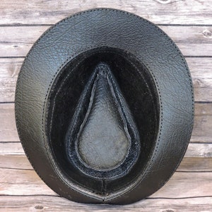 K&ouml;nnte beinhalten: Schwarzer Lederhut im Fedora-Stil mit einer gen&auml;hten Naht um den Rand. Der Hut ist auf links gedreht und zeigt das schwarze Lederfutter.