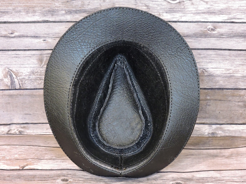 K&ouml;nnte beinhalten: Schwarzer Lederhut im Fedora-Stil mit einer gen&auml;hten Naht um den Rand. Der Hut ist auf links gedreht und zeigt das schwarze Lederfutter.