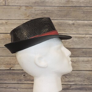 K&ouml;nnte beinhalten: Ein schwarzer Fedora-Hut mit rotem Band und einer Kroko-Pr&auml;gung.