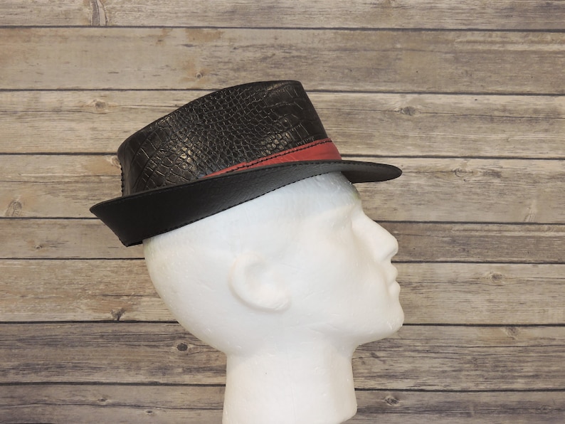 K&ouml;nnte beinhalten: Ein schwarzer Fedora-Hut mit rotem Band und einer Kroko-Pr&auml;gung.