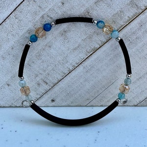 May include: A black elastic bracelet with a silver clasp and blue, green, and gold beads.