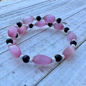 May include: A pink and white beaded bracelet with black accents. The beads are oval shaped and have a glossy finish.