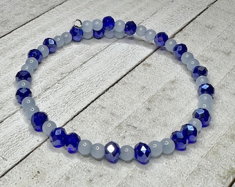 May include: A blue and white beaded bracelet with a silver clasp. The bracelet is made of small, faceted glass beads.