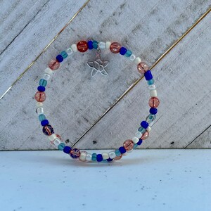 May include: A beaded bracelet with a silver starfish charm. The bracelet is made with white, blue, and pink beads.