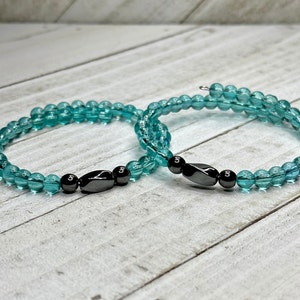May include: Two turquoise beaded bracelets with black magnetic clasps. The bracelets are layered on top of each other.